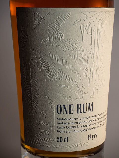 Nahaufnahme des Etiketts der ONE RUM No. 1 Flasche, mit einer feinen Prägung tropischer Pflanzenmotive. Das elegante Design unterstreicht die Exklusivität dieses 14 Jahre gereiften Single Cask Vintage Rums.