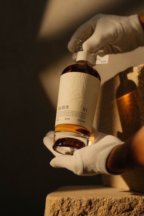 Hochwertige Flasche ONE RUM No. 1, 14 Jahre gereift, mit einem Alkoholgehalt von 52,1%, gehalten in weißen Handschuhen. Die Szene betont die Exklusivität und hohe Qualität des Single Cask Vintage Rums.