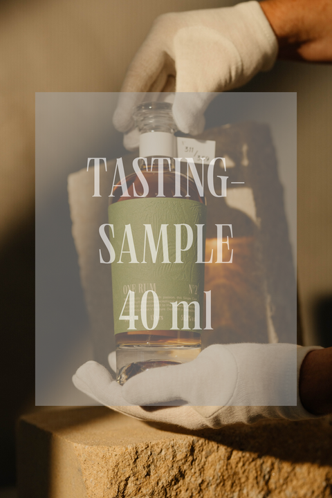 Verkostungsprobe von ONE RUM, 40 ml, die von einer behandschuhten Hand gehalten wird. Die grüne Flasche „No. 2“ steht für einen limitierten und hochwertigen Single Cask Rum.