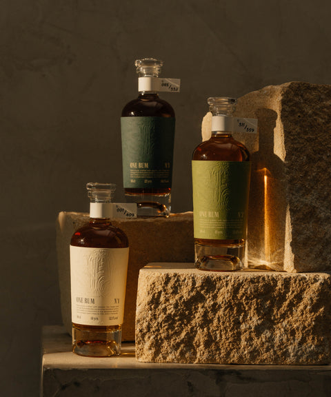 Drei Flaschen ONE RUM – No. 1, No. 2 und No. 3 – stilvoll auf Steinpodesten arrangiert. Die limitierte Single Cask Kollektion in verschiedenen Farben und Altersangaben symbolisiert die Exklusivität und handwerkliche Qualität des Rums.