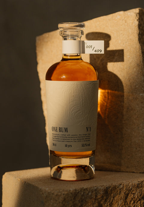 ONE RUM No. 1 Flasche auf einem Stein, golden beleuchtet. Die dezente Prägung des Etiketts und die Seriennummer 001/409 zeigen die kunstvolle Verarbeitung und Exklusivität dieser limitierten Rarität.