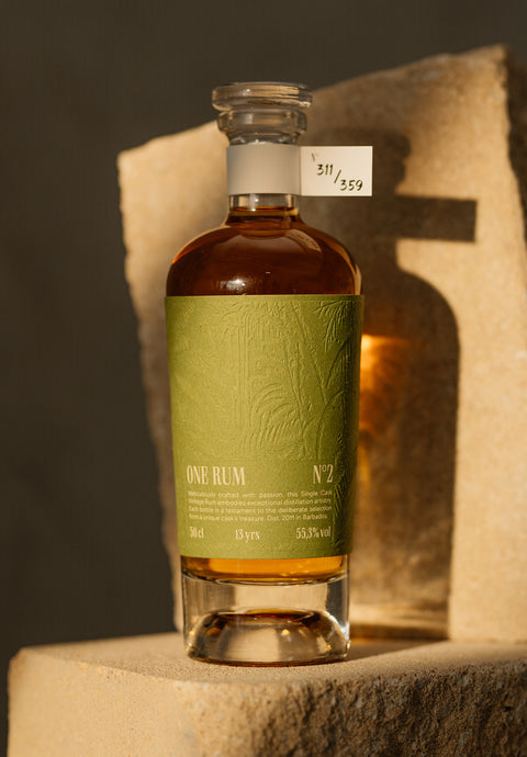 ONE RUM No. 2 Flasche, 13 Jahre gereift, mit grünem Etikett und Nummerierung 311/359, stilvoll auf einem Stein präsentiert. Der Single Cask Rum mit einem Alkoholgehalt von 55,3% vol. verkörpert Exklusivität und handwerkliche Perfektion.