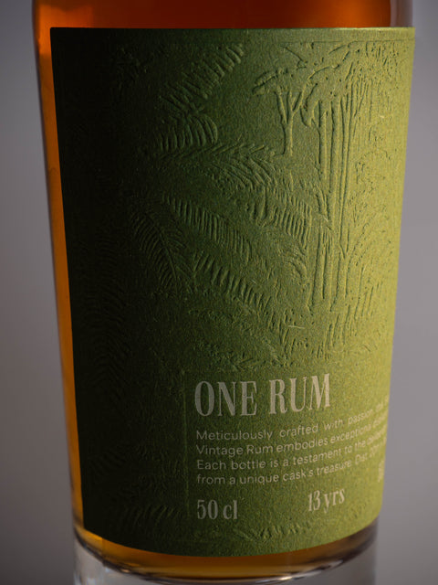 Detailaufnahme des Etiketts der ONE RUM No. 2 Flasche, geprägt mit tropischen Pflanzenmotiven auf grünem Hintergrund. Dieser limitierte Single Cask Rum ist 13 Jahre gereift und repräsentiert höchste Handwerkskunst.