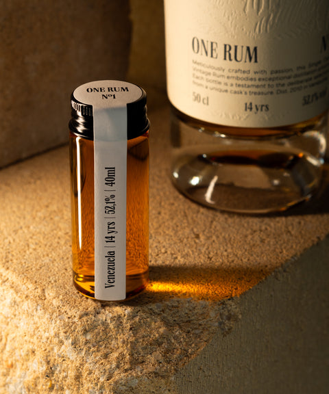 Probefläschchen ONE RUM No1 mit Panama Rum, 22 Jahre gereift und 60,1% Alkoholgehalt, vor einer größeren ONE RUM Flasche präsentiert. Die Szene zeigt den limitierten und exklusiven Charakter dieses Single Cask Vintage Rums.