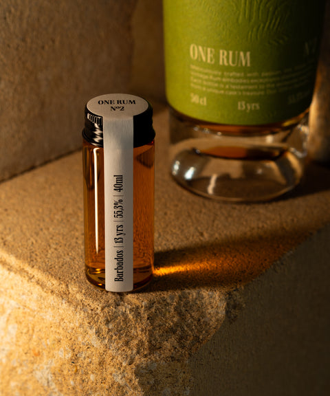 ONE RUM No2 Probefläschchen der Sorte Barbados, 13 Jahre gereift, mit 55,3% Alkoholgehalt, vor einer größeren ONE RUM Flasche im edlen Design. Die Aufnahme unterstreicht die besondere Auswahl an Single Cask Rums von ONE RUM.